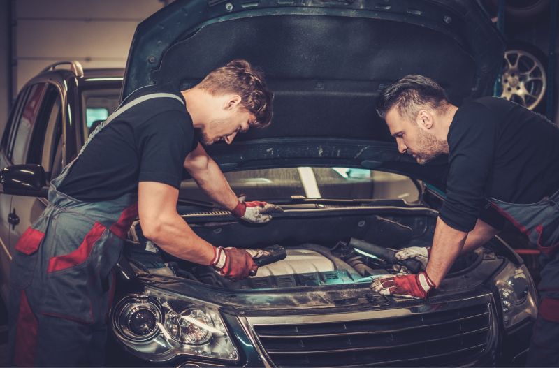 Zwei Kfz-Mechaniker inspizieren Motorraum eines PKWs